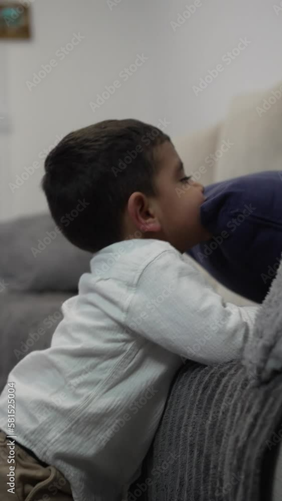 Vertical video of an autistic child coughing while leaning on the living room sofa playing at chewing on a blue cushion. Vertical video of an autistic child coughing while leaning on the living room sofa playing at chewing on a blue cushion.