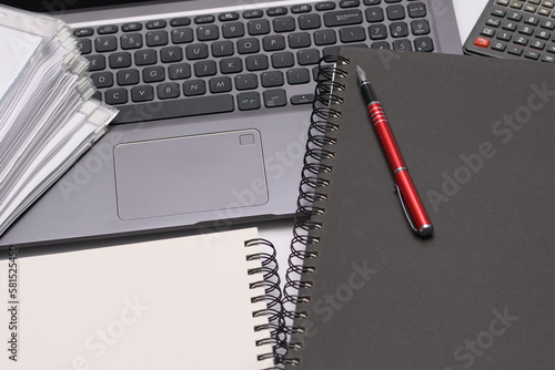 Laptop, notes, długopis i stos dokumentów - biurko w pracy