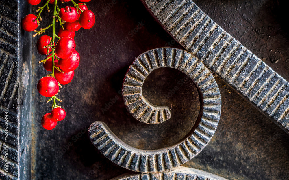 Black, rough forged iron surface with curved shaped decor and a bunch of bright red peppercorn fruits. Black, rough forged iron surface with curved shaped decor and a bunch of bright red peppercorn fruits.