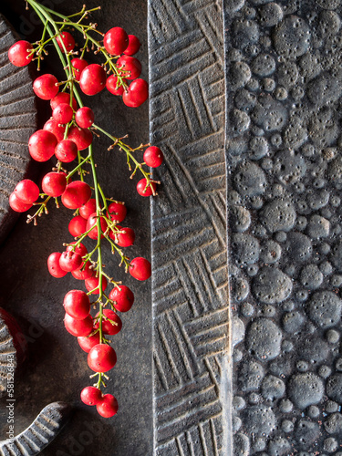 Black, rough forged iron surface with space for text or logo, and a bunch of bright red peppercorn fruits.