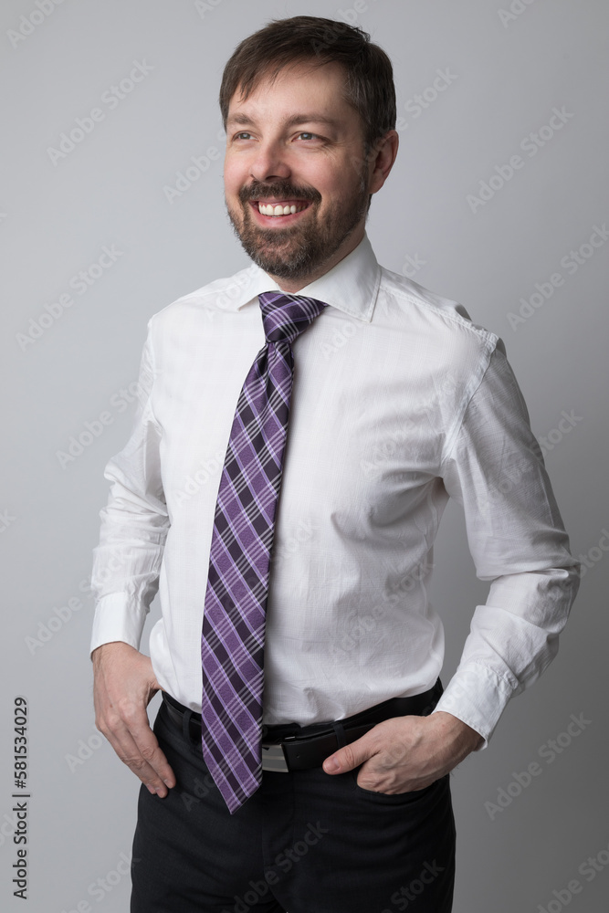 Studio portrait of a caucasian man in his 40s smiling. He is wearing a white buttoned up shirt and dark dress pants. He is a business executive. The background is grey. Studio portrait of a caucasian man in his 40s smiling. He is wearing a white buttoned up shirt and dark dress pants. He is a business executive. The background is grey.