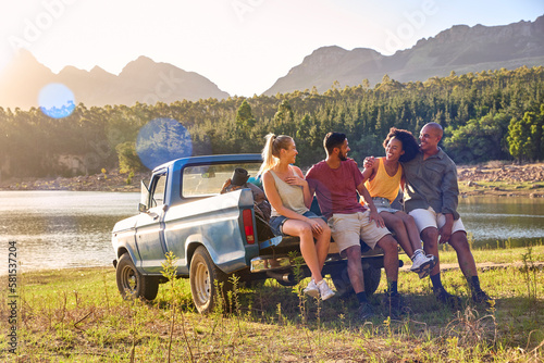 Group Of Friends With Backpacks In Pick Up Truck On Road Trip By Lake And Mountains photo