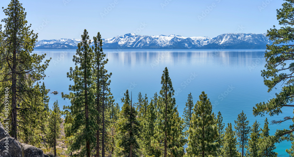 Blue Mountain Lake - A sunny Spring day view of serene blue Lake Tahoe, surrounded by snow-capped peaks and dense pine forest, California-Nevada, USA.