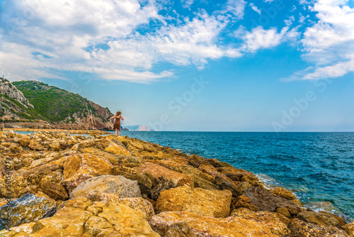 Young woman or girl on a rocky seashore wearing dress and straw hat in Alanya resort, Turkey