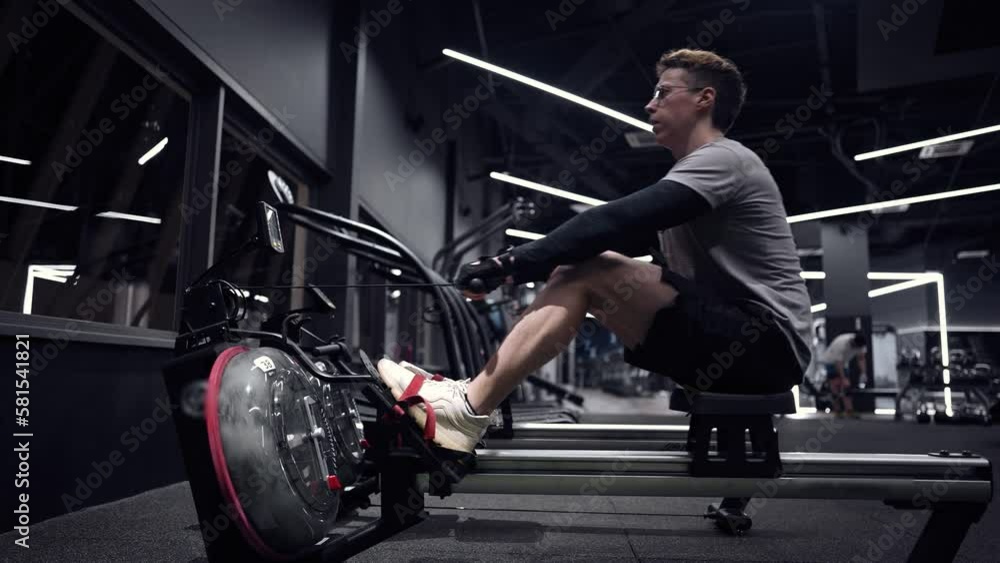 the guy trains on Rowing Machines Cardio Training: Sports Outdoors slow motion modern simulators the guy trains on Rowing Machines Cardio Training: Sports Outdoors slow motion modern simulators
