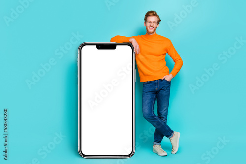 Photo of cool pretty young man wear orange pullover spectacles modern device empty space isolated teal color background