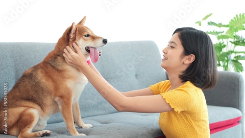 Fotografie Happy young Asian woman playing and stroking the head of her pet puppy cute dog