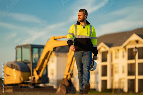 Worker in helmet on site construction. Man excavator bulldozer worker. Construction driver worker with excavator on the background. Construction worker with tractor or construction at building.