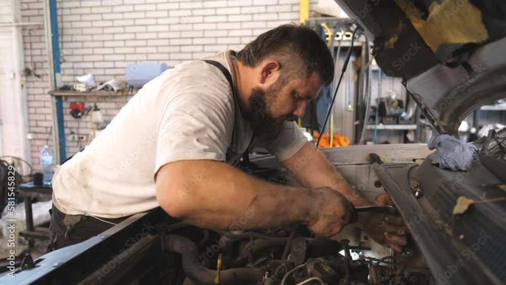 Repairman fixing engine of car using wrench at workshop or service. Professional auto mechanic works under hood of vehicle. Man repair automobile motor at garage. Concept of maintenance and diagnostic Repairman fixing engine of car using wrench at workshop or service. Professional auto mechanic works under hood of vehicle. Man repair automobile motor at garage. Concept of maintenance and diagnostic