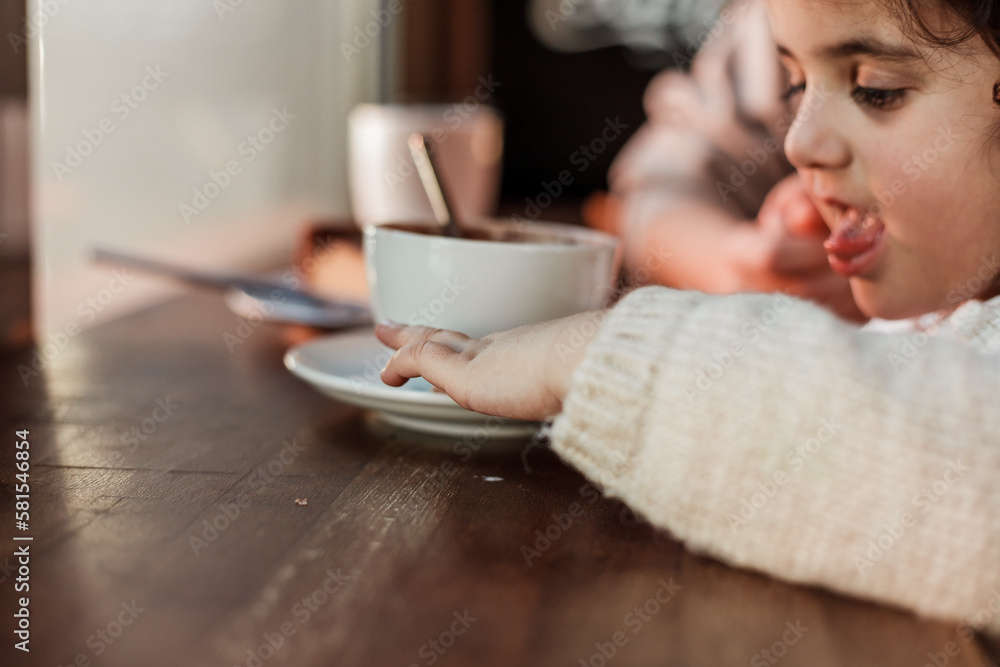 Beautiful young red-haired mother with cute curly-haired daughter are drink hot cocoa with cake in a cozy cafe. Beautiful young red-haired mother with cute curly-haired daughter are drink hot cocoa with cake in a cozy cafe.
