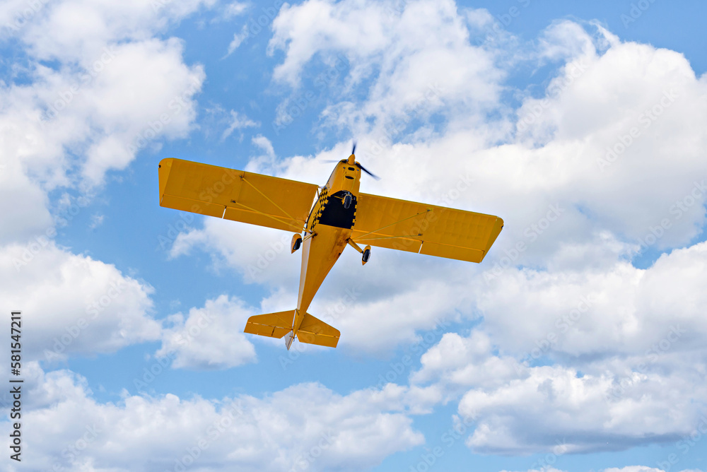 Yellow single-engine ultralight airplane flying in the blue sky with white clouds Yellow single-engine ultralight airplane flying in the blue sky with white clouds