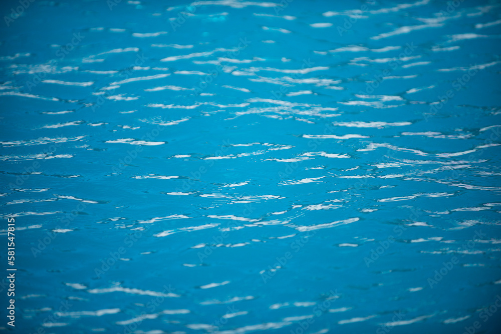 Water background. Blue water, ripples and highlights. Texture of water surface and tiled bottom.