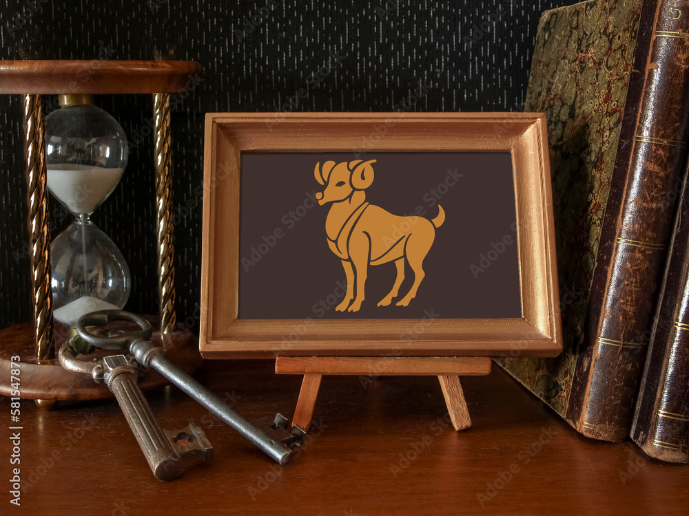 Zodiac sign Aries in a frame on a stand in a composition of hourglasses, keys, old books