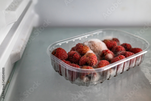 Moldy raspberries in a plastic basket inside a refrigerator. Food past its expiration date, spoiled food.