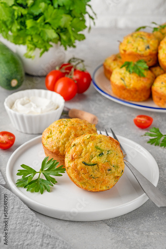 Homemade zucchini muffins with cheese, garlic and herbs on a plate on a gray concrete background. Vegetarian dish. Copy space.