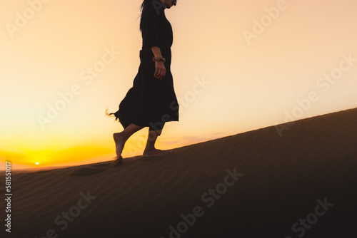 Woman black dress walking in the Dubai desert sand dunes with footsteps in the sand during sunset, woman walk golden sand summer evening,Dubai Safari Emirates holliday vacation photo