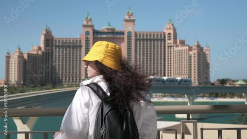 a girl stands in front of the Atlantis Hotel, The Palm in Dubai, a woman stands in front of a passing monorail in Dubai, slow motion