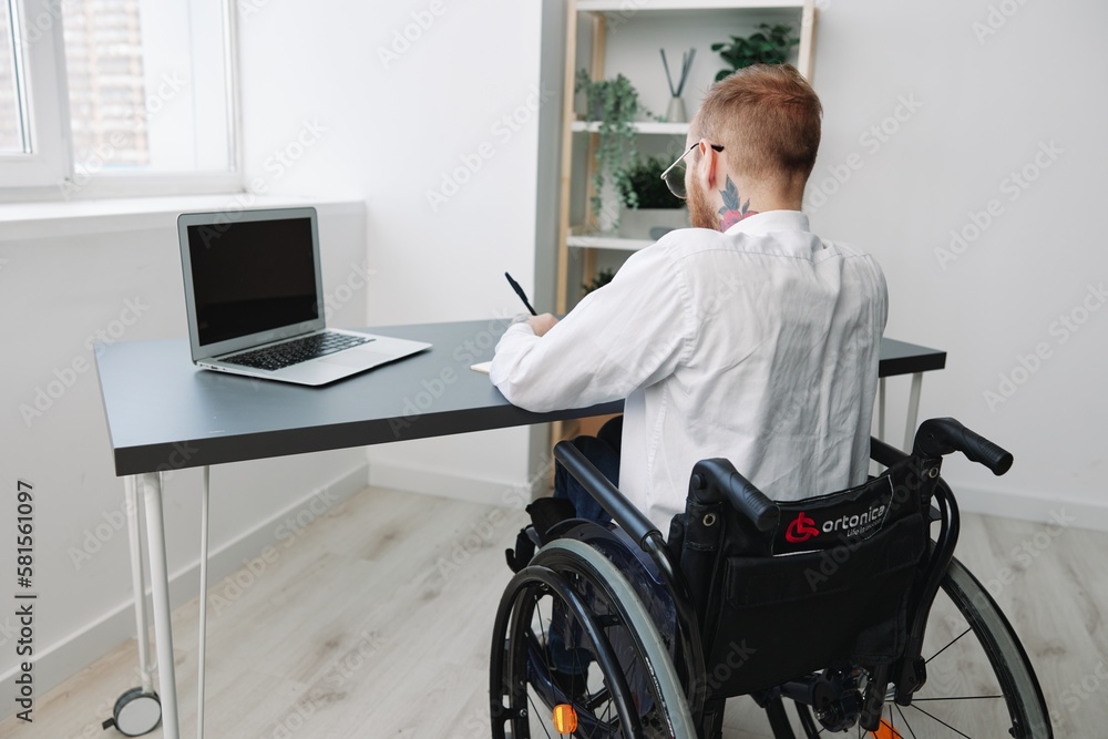 man wheelchair businessman with tattoos in the office works at a laptop online, business process from the back, copy space, integration into society, the concept of working a person with disabilities man wheelchair businessman with tattoos in the office works at a laptop online, business process from the back, copy space, integration into society, the concept of working a person with disabilities