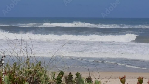 Beautiful remote beach in Portugal with big waves and dune grass in the foreground.