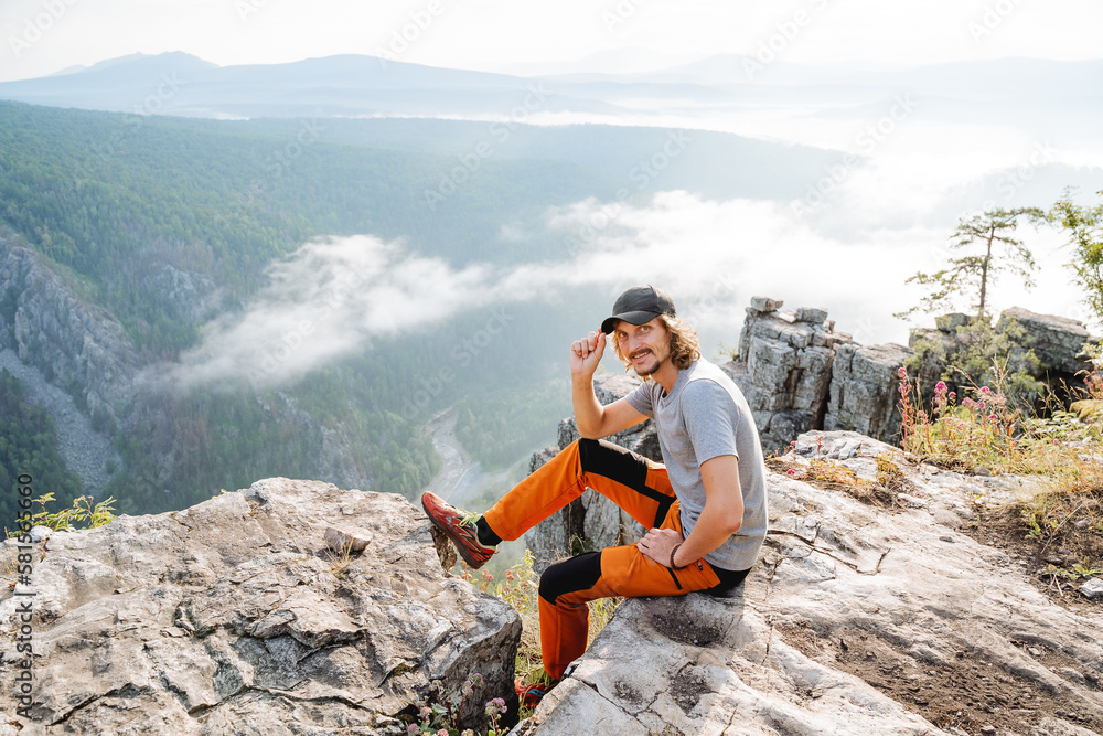 Φωτογραφία A guy in a tourist cap sits on the edge of a cliff, a tourist climb into the mountains, a man rests in nature high in the mountains, a guide to the area, a blogger on a halt