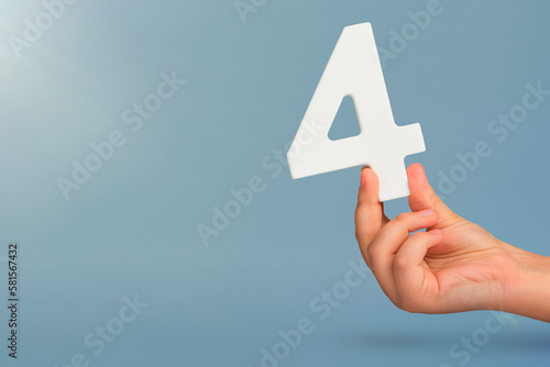 number four in hand. Hand holding white number 4 on blue background with copy space. Concept with number four. Birthday 4 years, fourth grade, four day work week photo