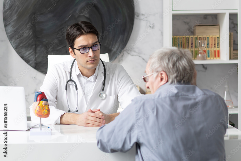 Aged man visiting young male doctor cardiologist in modern clinic Aged man visiting young male doctor cardiologist in modern clinic