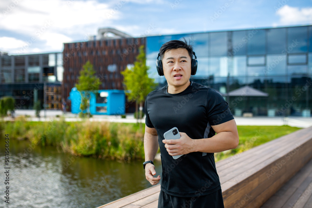An asian man running and exercising in park with music with headphones and phone outdoors. Young athlete, outdoor runner and motivation for fitness, energy and healthy exercise.