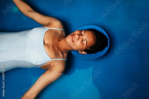 Middle-aged African American woman floating in tank filled with dense salt water used in meditation, therapy and alternative medicine.