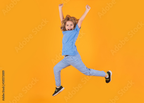 Full length of excited kid jumping. Energetic kid boy jumping and raising hands up on isolated studio background. Full length body size photo of jumping high child boy, hurrying up.