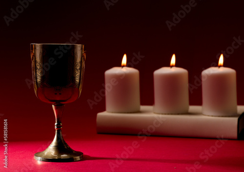 christian chalice on bible by burning candles red background