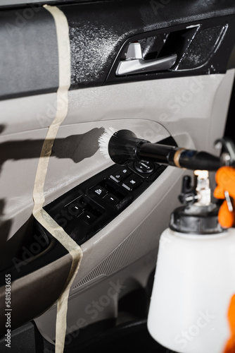 Car detailing with tornador cleaning gun with high pressure air pulse. Cleaner is washing car door card panel and spraying detergent from tornador gun.