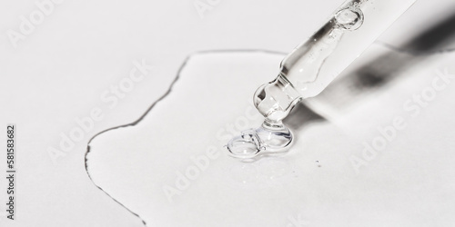 Drop of facial serum or oil with bubbles pouring from transparent pipette on grey background. Web banner for anti aging cosmetic product advertising. Liquid gel with retinol closeup. Front view. photo