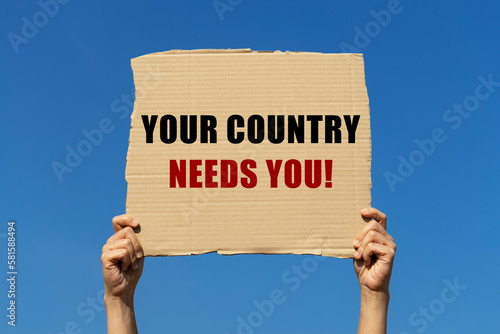 Photo Your country needs you text on box paper held by 2 hands with isolated blue sky background