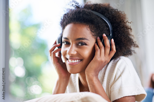 Time to kick back and relax. a young woman wearing headphones listening to music at home.