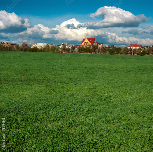 beautiful green field in spring and settlement with buildings on horizon