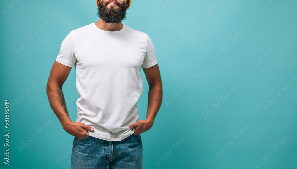Portrait of handsome, young, stunning, perfect bearded guy wearing a white blank t-shirt stands against turquoise background. T-shirt template. Portrait of handsome, young, stunning, perfect bearded guy wearing a white blank t-shirt stands against turquoise background. T-shirt template.