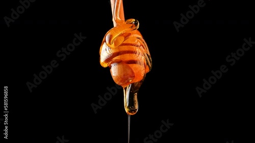 Close up fresh thick fluid honey pouring from wooden dipper spoon over black background