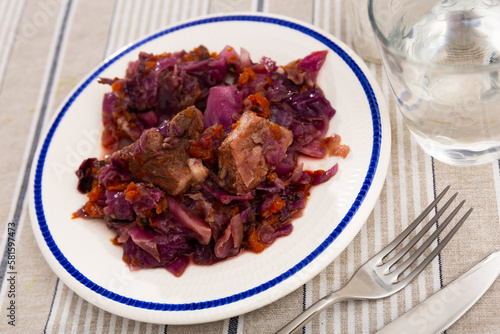 Cabbage stew whith pork meat and red carrots on plate. Hearty rustic russian food
