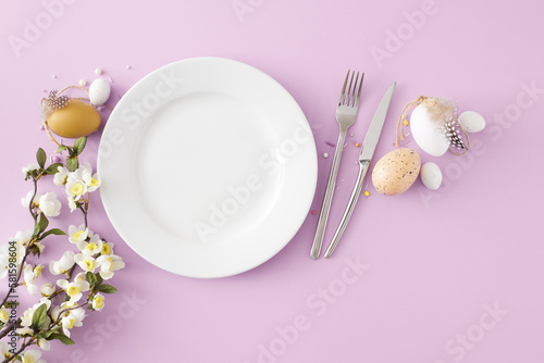 Easter decoration concept. Top view composition of empty plate with cutlery fork knife colorful easter eggs and cherry blossom branch on isolated lilac background with blank space