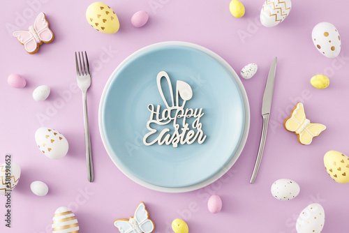 Easter decor idea. Top view photo of plate with inscription happy easter cutlery colorful eggs and butterfly shaped cookies on isolated violet background