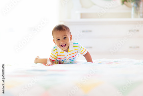 Baby boy playing on bed in sunny nursery