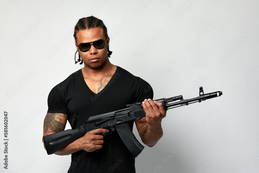 African American in a black jacket with a machine gun in his hands and sunglasses, on a white background. African American in a black jacket with a machine gun in his hands and sunglasses, on a white background.