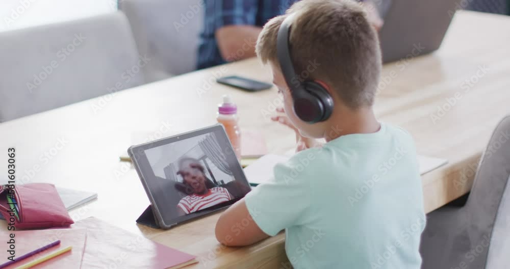 Happy caucasian boy sitting at table and using tablet for video call, slow motion Happy caucasian boy sitting at table and using tablet for video call, slow motion