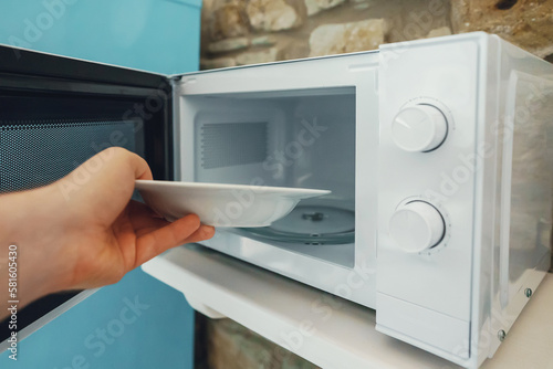 Man putting plate with food to heat in the microwave.