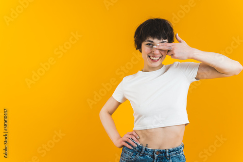 Smiling woman covering one of her eyes with two fingers and resting the other hand on her hip. Bright background. High quality photo © PoppyPix
