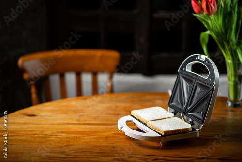 Foto Sandwich maker with bread toast on wooden table