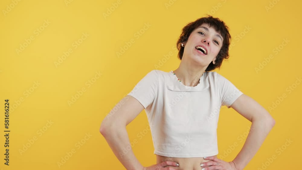 Female model smiling during photo session. Casually-dressed short-haired girl biting her lower lip. Medium closeup shot. Copy space over yellow background. High quality 4k footage Female model smiling during photo session. Casually-dressed short-haired girl biting her lower lip. Medium closeup shot. Copy space over yellow background. High quality 4k footage
