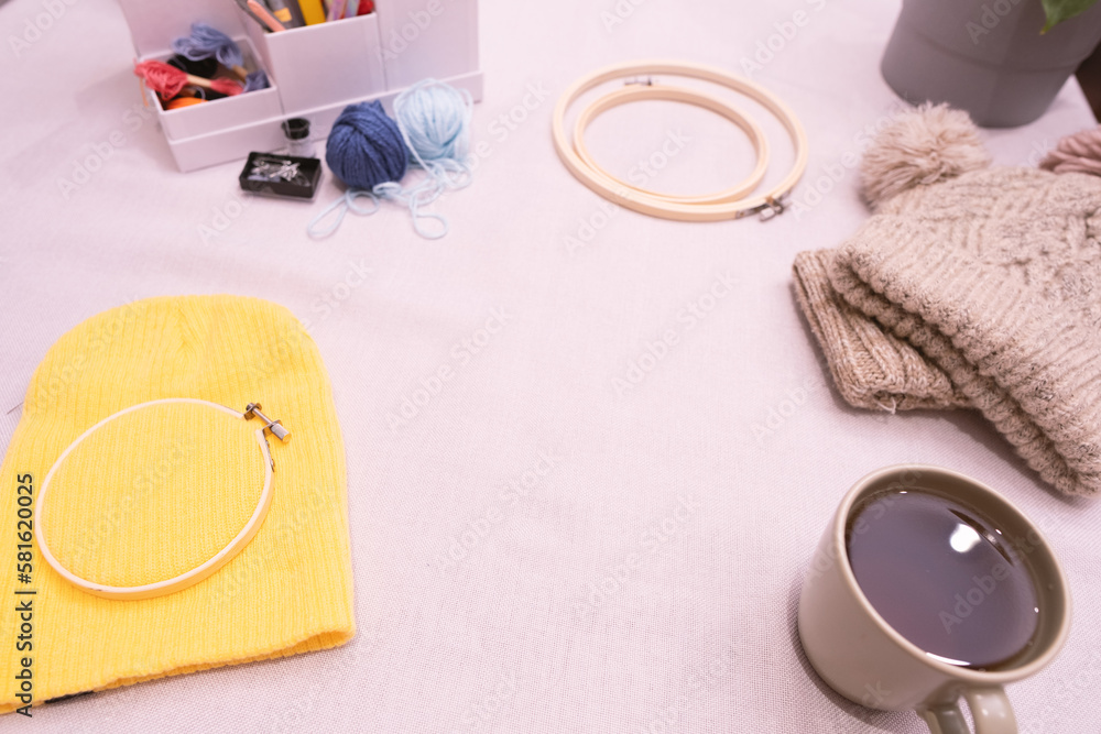 Yellow wool hat, wool yarn, embroidery hoop, coffee cup, tools Yellow wool hat, wool yarn, embroidery hoop, coffee cup, tools