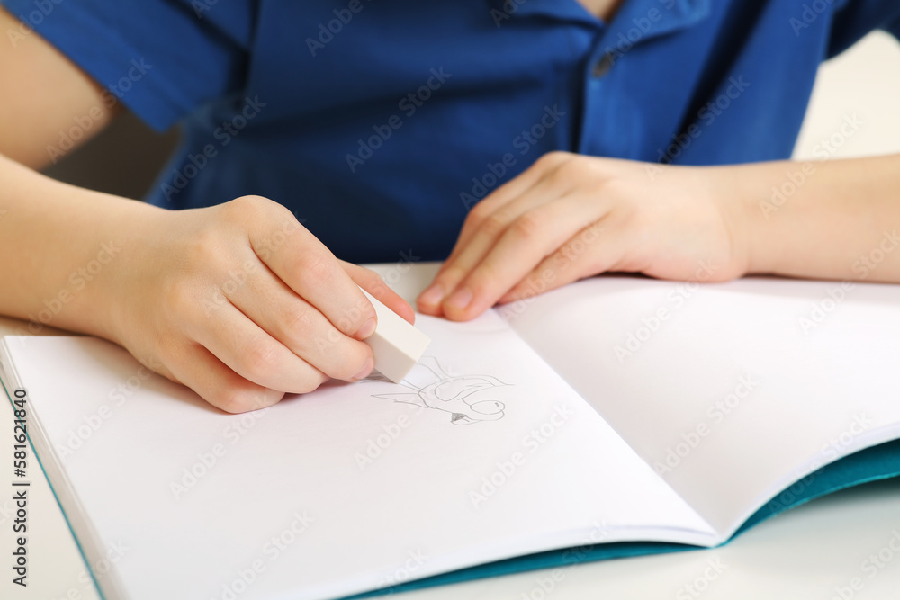 Boy erasing mistake in his notebook at white desk, closeup Boy erasing mistake in his notebook at white desk, closeup