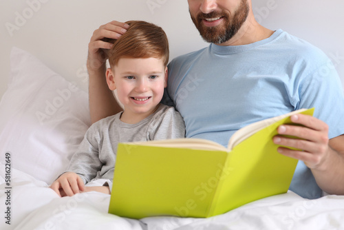 Father reading book with his child on bed at home